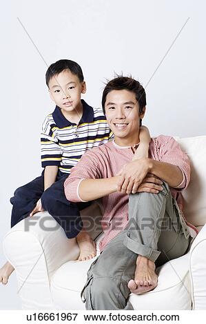 Portrait of a mid adult man sitting in an armchair with his son beside him View Large Photo Image Stock Photo - Portrait of a mid adult man sitting in an armchair with his son beside him. Fotosearch