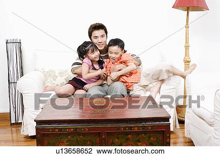 Portrait of a mid adult man sitting on a couch and hugging his son and daughter View Large Photo Image Stock Image - Portrait of a mid adult man sitting on a couch and hugging his son and daughter. Fotosearch