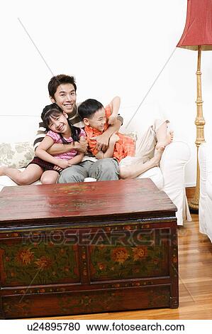 Portrait of a mid adult man sitting on a couch and hugging his son and daughter View Large Photo Image Stock Image - Portrait of a mid adult man sitting on a couch and hugging his son and daughter. Fotosearch