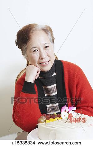 Picture - Portrait of a senior woman sitting in front of a birthday cake smiling. Fotosearch