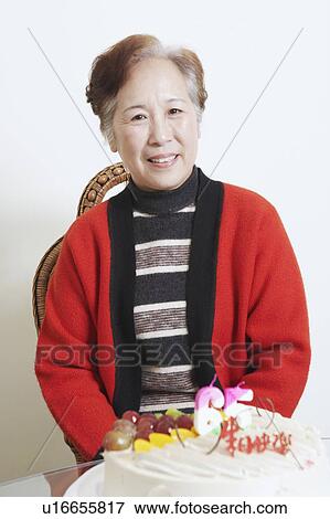 Stock Photo - Portrait of a senior woman sitting in front of a birthday cake smiling. Fotosearch