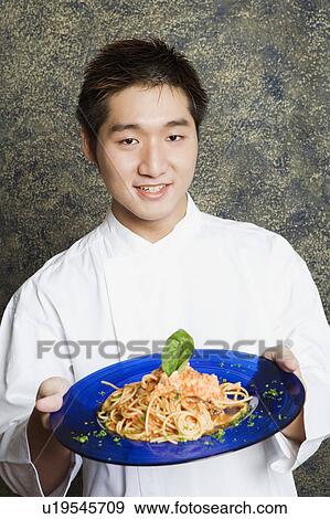 Stock Photo - Portrait of a waiter holding a plate of noodles. Fotosearch