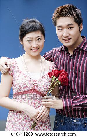 Stock Photo - Portrait of a young couple holding a bunch of roses and smiling. Fotosearch
