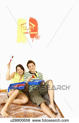 Stock Photo - Portrait of a young couple holding paintbrushes and smiling. Fotosearch