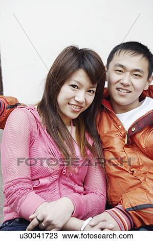 Stock Image - Portrait of a young couple sitting together smiling. Fotosearch
