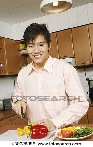 Stock Photograph - Portrait of a young man cutting vegetables at a kitchen counter. Fotosearch