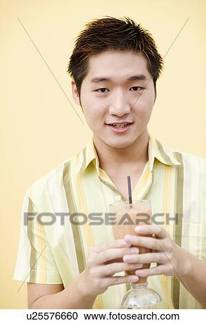 Portrait of a young man holding a glass of milkshake View Large Photo Image Stock Image - Portrait of a young man holding a glass of milkshake. Fotosearch