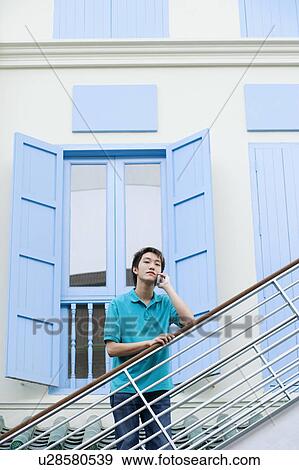 Stock Photo - Portrait of a young man leaning against a staircase and talking on a mobile phone. Fotosearch