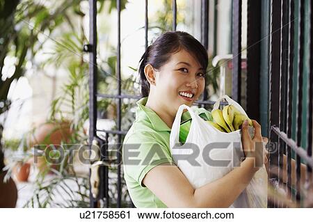 Stock Image - Portrait of a young woman carrying a plastic bag with bananas. Fotosearch