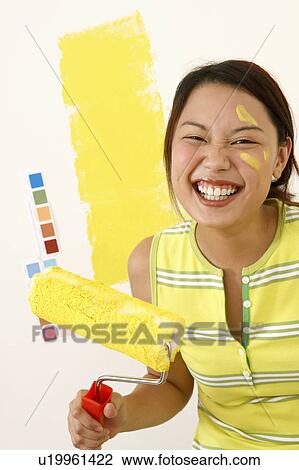 Stock Image - Portrait of a young woman holding a paint roller. Fotosearch