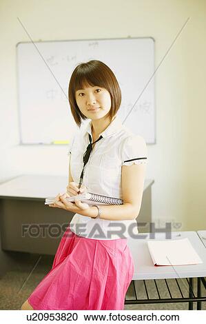 Portrait of a young woman holding a spiral notebook and leaning against a desk View Large Photo Image Stock Image - Portrait of a young woman holding a spiral notebook and leaning against a desk. Fotosearch