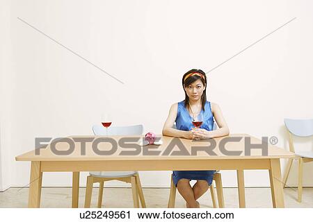 Stock Image - Portrait of a young woman holding a glass of wine and sitting on a chair. Fotosearch