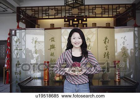 Stock Photography - Portrait of a young woman holding a bowl of incense sticks. Fotosearch