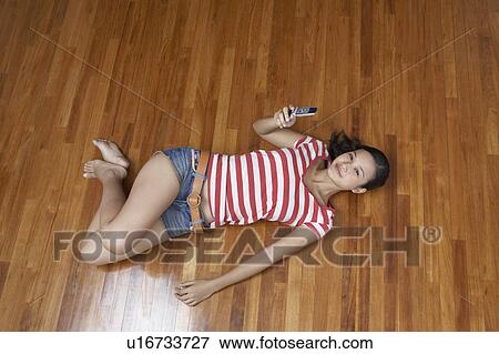 Stock Photo - Portrait of a young woman lying on a hardwood floor and holding a mobile phone. Fotosearch