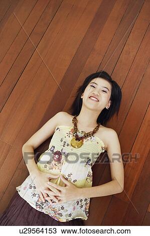 Stock Image - Portrait of a young woman lying on the floor and smiling. Fotosearch