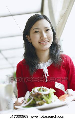 Stock Photo - Portrait of a young woman seated at the table in a restaurant smiling. Fotosearch