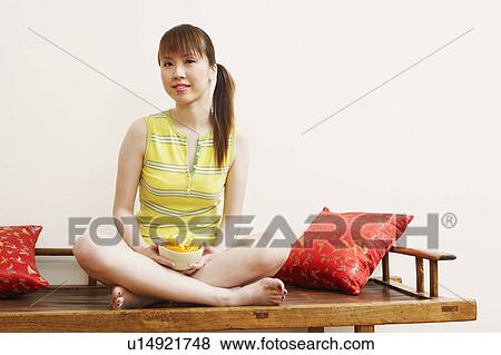 Stock Photo - Portrait of a young woman sitting on a bench and holding orange slices in a bowl. Fotosearch