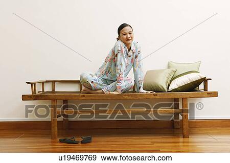 Portrait of a young woman sitting on a bench and smiling View Large Photo Image Stock Photo - Portrait of a young woman sitting on a bench and smiling. Fotosearch