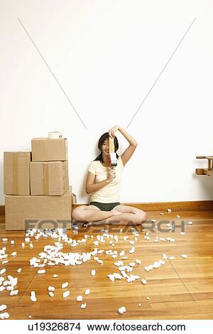 Picture - Portrait of a young woman sitting on the floor and holding a tape dispenser. Fotosearch