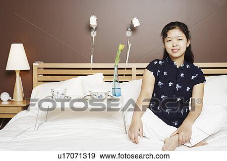 Portrait of a young woman sitting on the bed smiling View Large Photo Image Stock Photo - Portrait of a young woman sitting on the bed smiling. Fotosearch