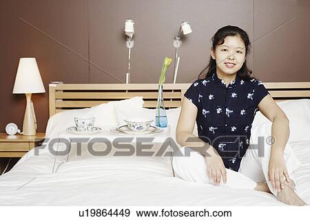 Stock Photo - Portrait of a young woman sitting on the bed smiling. Fotosearch