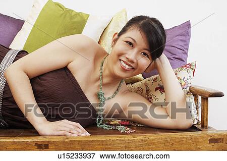 Stock Photo - Portrait of a young woman smiling and lying on a bench. Fotosearch