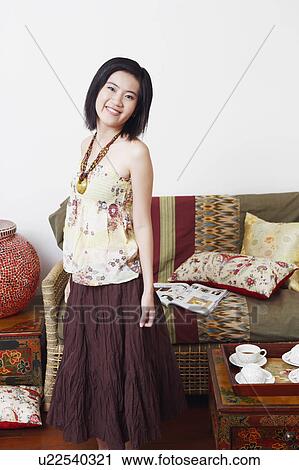 Stock Image - Portrait of a young woman standing in a room and smiling. Fotosearch