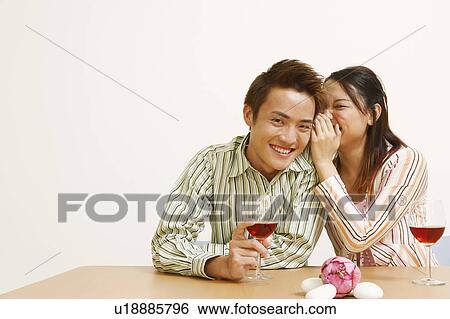 Stock Photograph - Portrait of a young woman whispering into a young man's ear. Fotosearch
