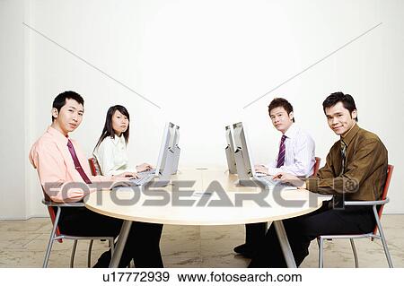 Stock Photo - Portrait of three businessmen with a businesswoman working on computers. Fotosearch