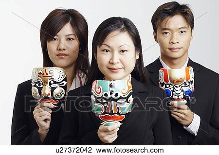 Stock Image - Portrait of two businesswomen and a businessman holding masks. Fotosearch