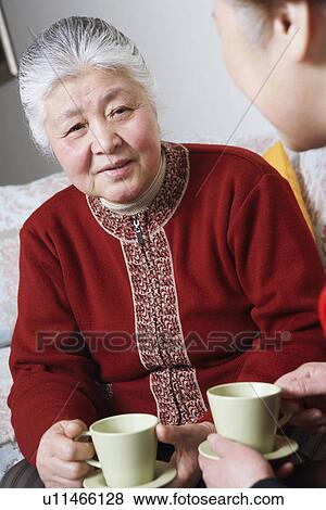 Stock Photo - Senior woman facing a woman holding a cup of tea. Fotosearch