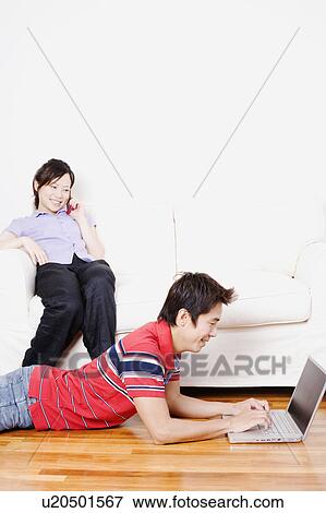 Side profile of a mid adult man using a laptop with a young woman talking on a mobile phone View Large Photo Image Stock Photo - Side profile of a mid adult man using a laptop with a young woman talking on a mobile phone. Fotosearch