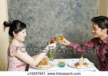 Stock Image - Side profile of a young couple toasting with champagne in a restaurant. Fotosearch