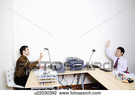 Stock Image - Two businessmen sitting face to face with their hands raised. Fotosearch