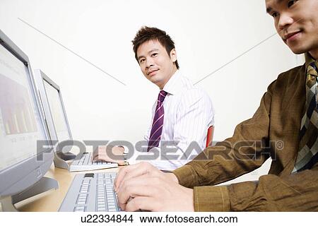 Picture - Two businessmen working on computers. Fotosearch