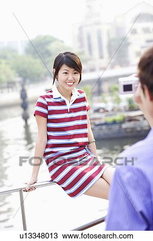 Stock Image - Young man taking a picture of a young woman. Fotosearch