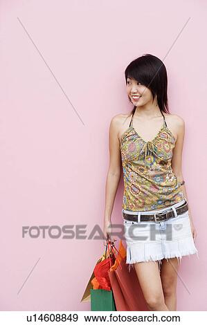 Young woman leaning against a wall and holding bags View Large Photo Image Stock Photo - Young woman leaning against a wall and holding bags. Fotosearch