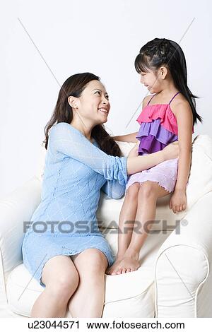 Stock Image - Young woman sitting in an armchair with her daughter and smiling. Fotosearch