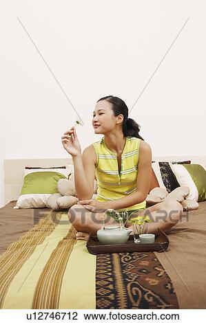 Stock Image - Young woman sitting on the bed and looking at a flower. Fotosearch