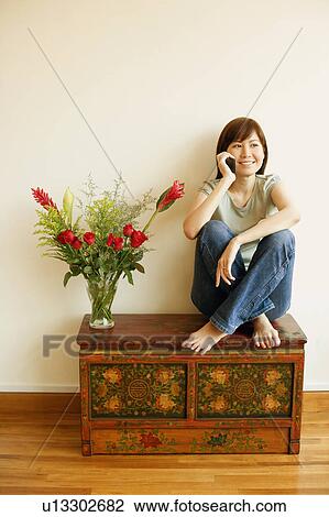 Stock Image - Young woman sitting on the table and talking on a mobile phone. Fotosearch