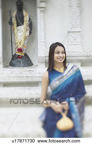 Stock Image - Young woman standing in front of a religious figure. Fotosearch