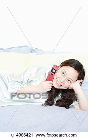 Young woman using a mobile phone on the bed View Large Photo Image Stock Image - Young woman using a mobile phone on the bed. Fotosearch