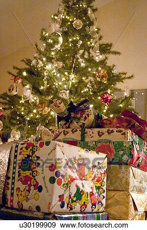 Stock Photo - Christmas presents piled high around the decorated evergreen tree. Fotosearch