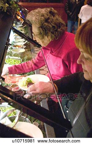 Stock Image - Women age 90 and 62 helping themselves at the salad bar. Fotosearch