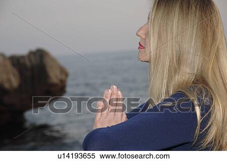 Stock Photography - Woman on a rocky sea coast, meditating cross-legged, profile. Fotosearch