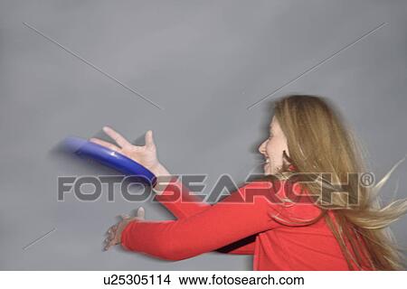 Picture - Woman playing with a frisbee, throwing and catching, in front of dark clouds. Fotosearch