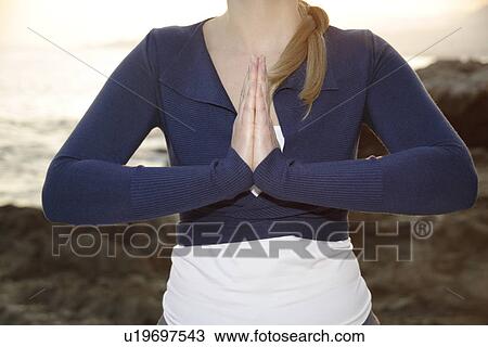 Stock Image - Woman standing at a rocky sea coast, meditating. Fotosearch