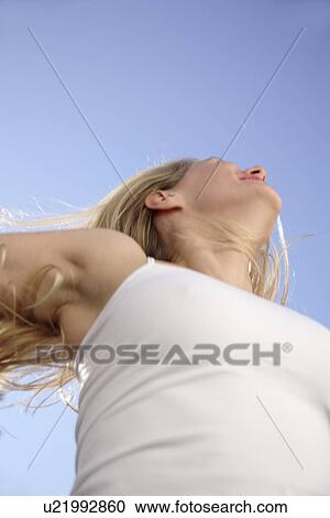 Stock Image - Woman stretching out arms in front of blue sky, low angle view. Fotosearch