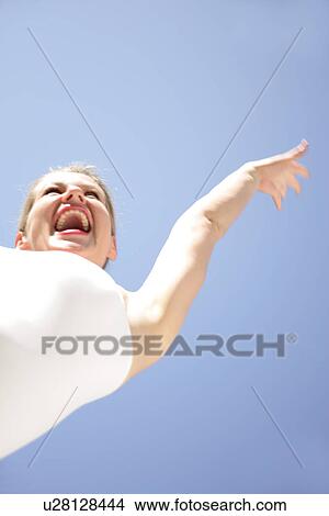 Picture - Young blond woman dancing, jumping and cheering at the beach, worm's eye view. Fotosearch