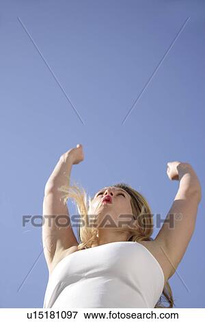 Stock Photo - Young blond woman dancing, jumping and cheering at the beach, worm's eye view. Fotosearch